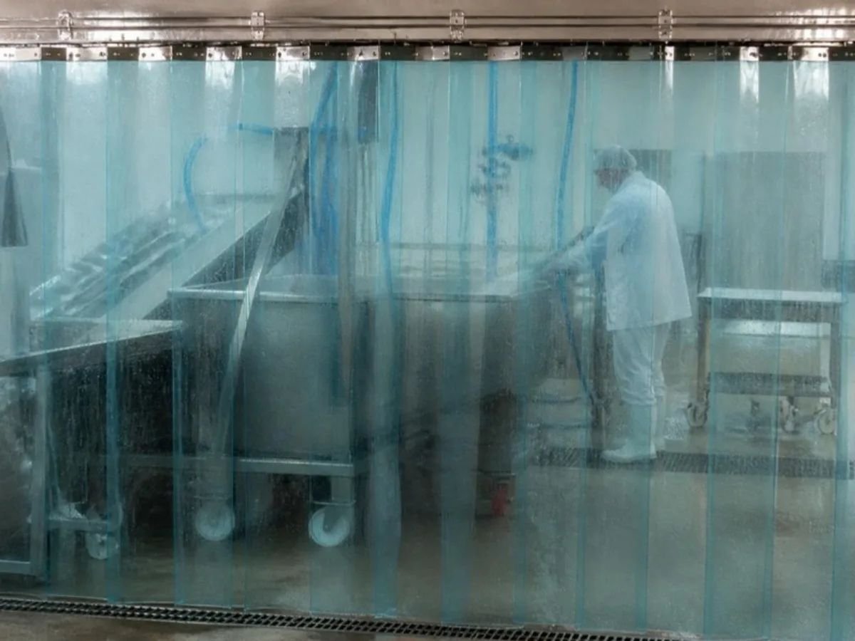 Clear washdown strip curtain containing spray while a worker cleans equipment behind it